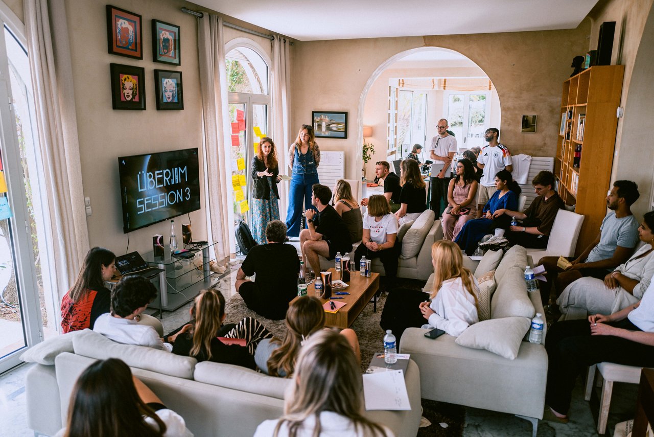 Spark Academy 2025 in Cannes: Two women present in front of an audience. The TV screen reads "ÜBERJAM SESSION 3", and colorful sticky notes cover the wall nearby.