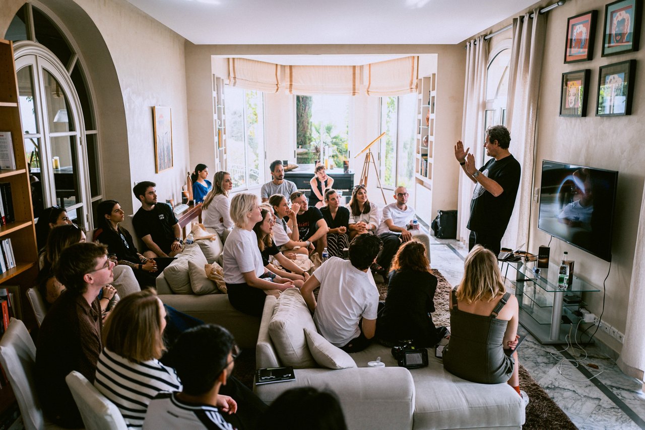 Spark Academy 2025 in Cannes: A group attentively listens to a speaker in the living room of a villa. The space is bright and comfortably furnished with sofas.