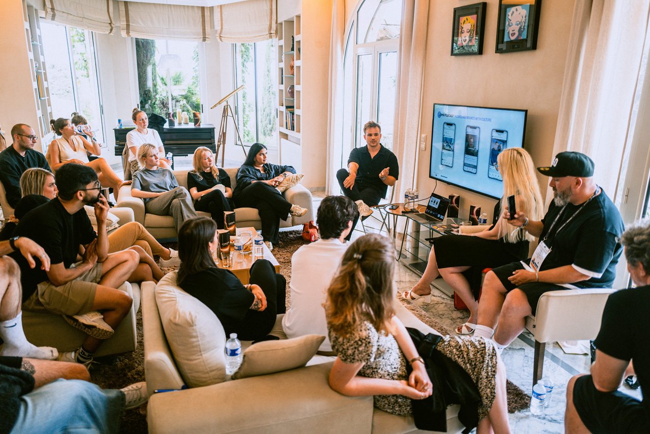 Spark Academy 2025 in Cannes: Presentation about branding and culture. A man speaks while two others sit beside him. A large screen displays mobile app mockups.
