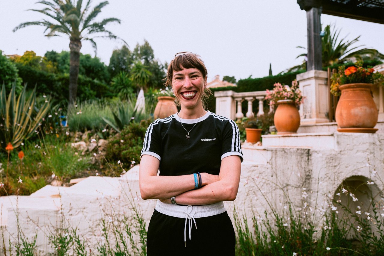 Spark Academy 2025 in Cannes: Smiling woman with bangs stands with arms crossed in front of a villa with palm trees and terracotta pots.