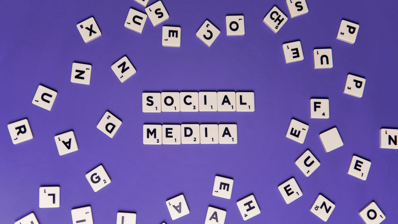 Weiße Buchstabensteine liegen verstreut auf lila Hintergrund, in der Mitte bilden sie die Worte „SOCIAL MEDIA“