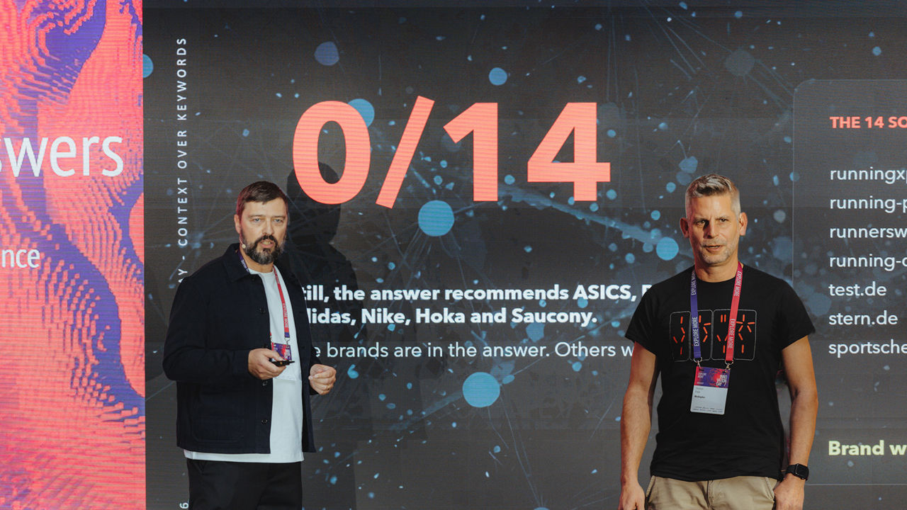 Two people (Stephan Kopp and Mika Riegger) are standing on a stage in front of a presentation slide on the topics of AI, search queries, and brand perception.