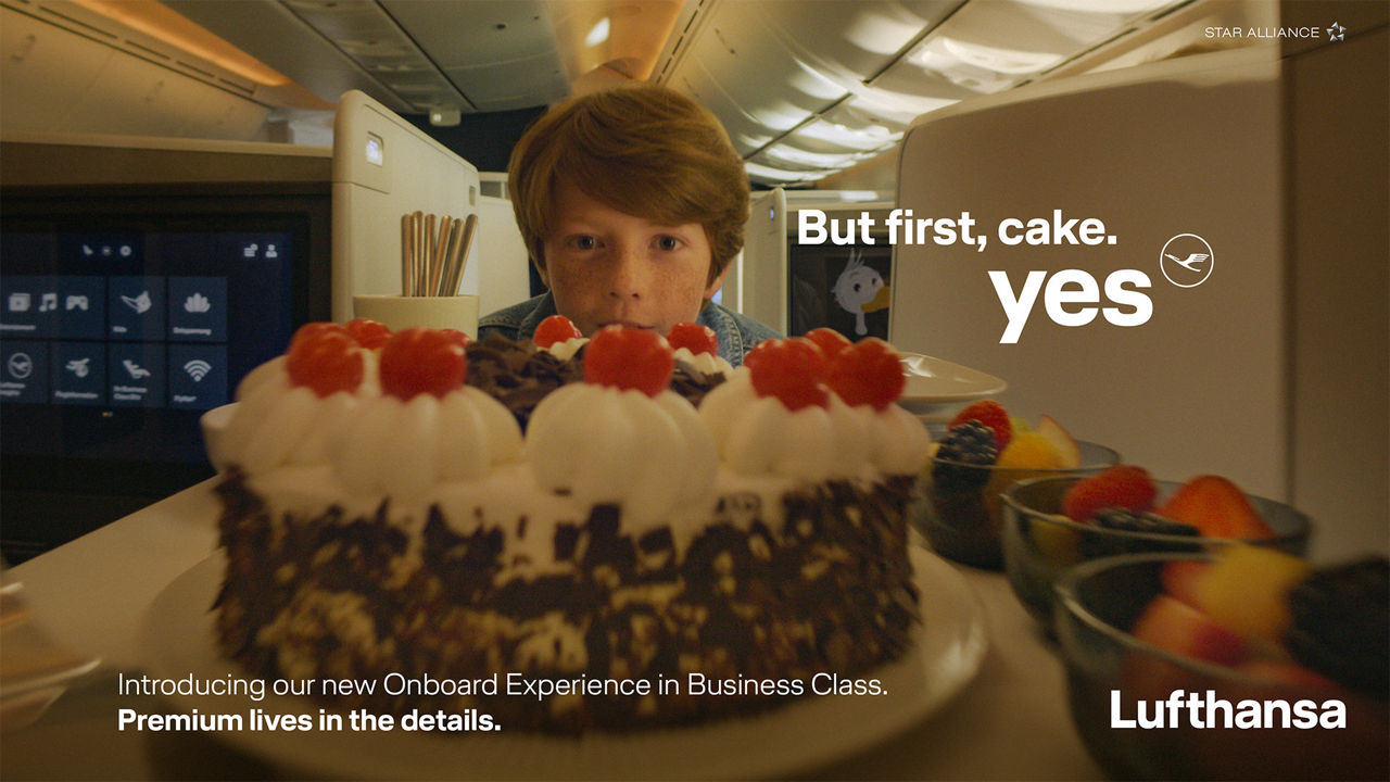 Lufthansa Business Class campaign visual showing a passenger-facing dessert service in the aircraft cabin. The image highlights the airline’s premium onboard dining experience and Business Class service offering.