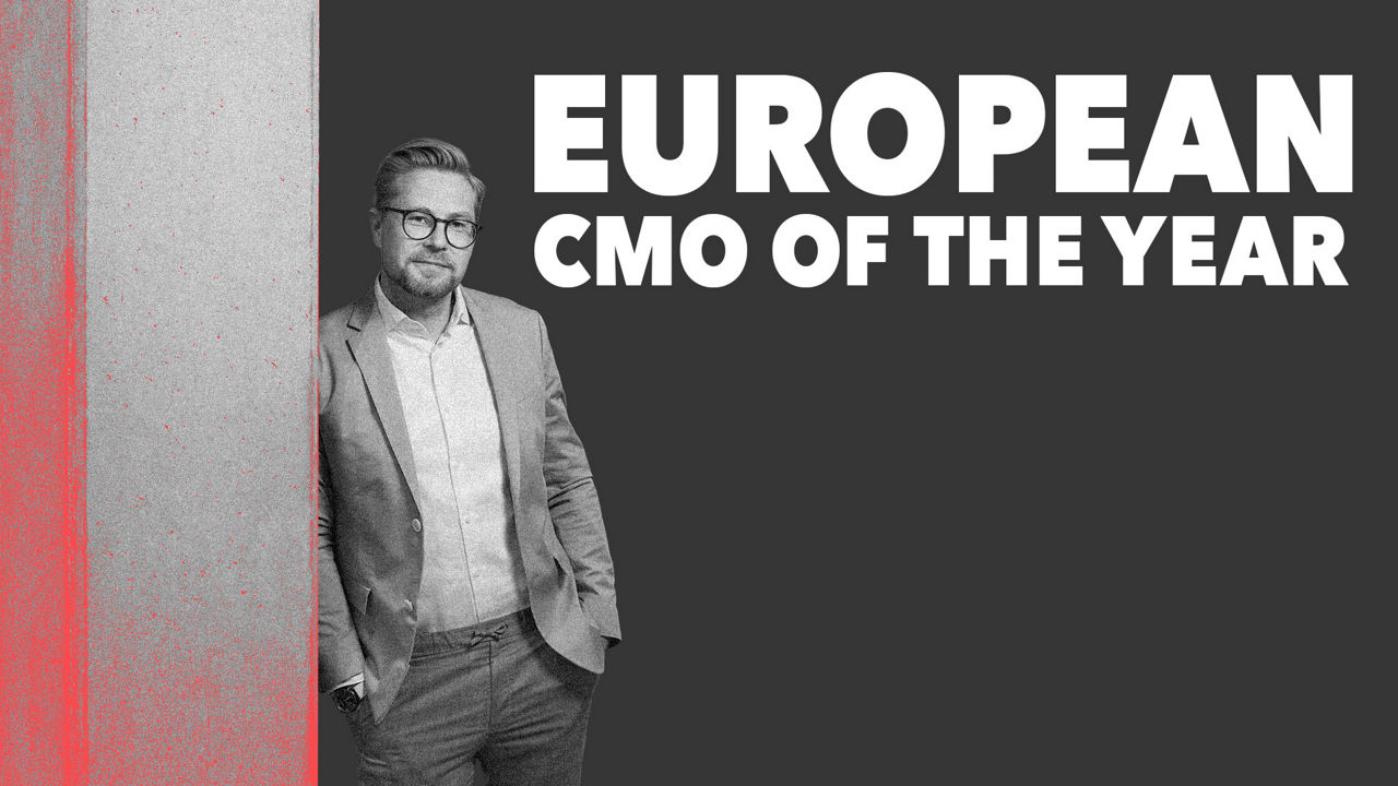 Schwarz-weißes Porträt von Felix Bartels mit Brille, Sakko und Hemd, der mit den Händen in den Hosentaschen vor dunklem Hintergrund steht.