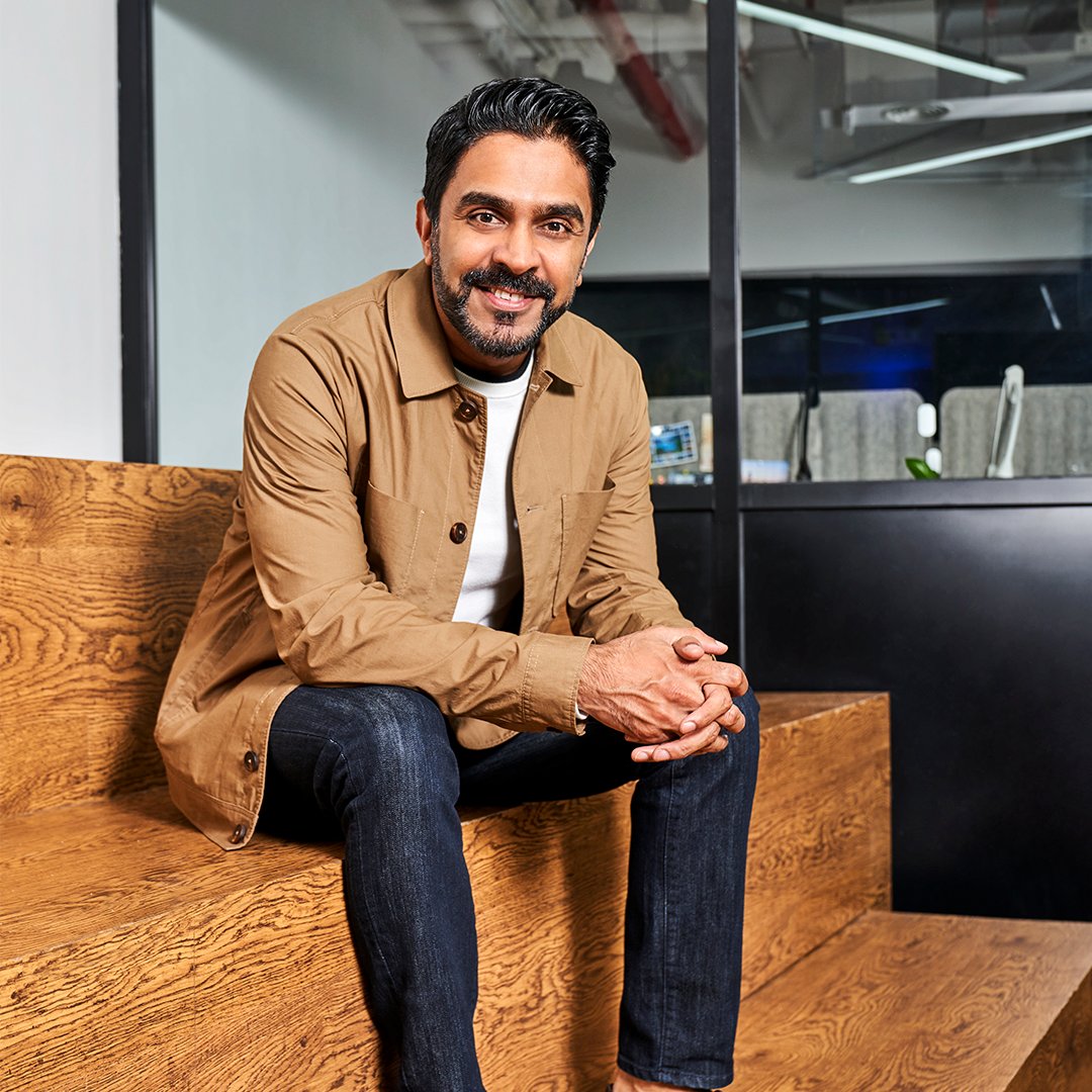 Azhar Siddiqui sitting on wooden steps in an office, smiling at the camera.
