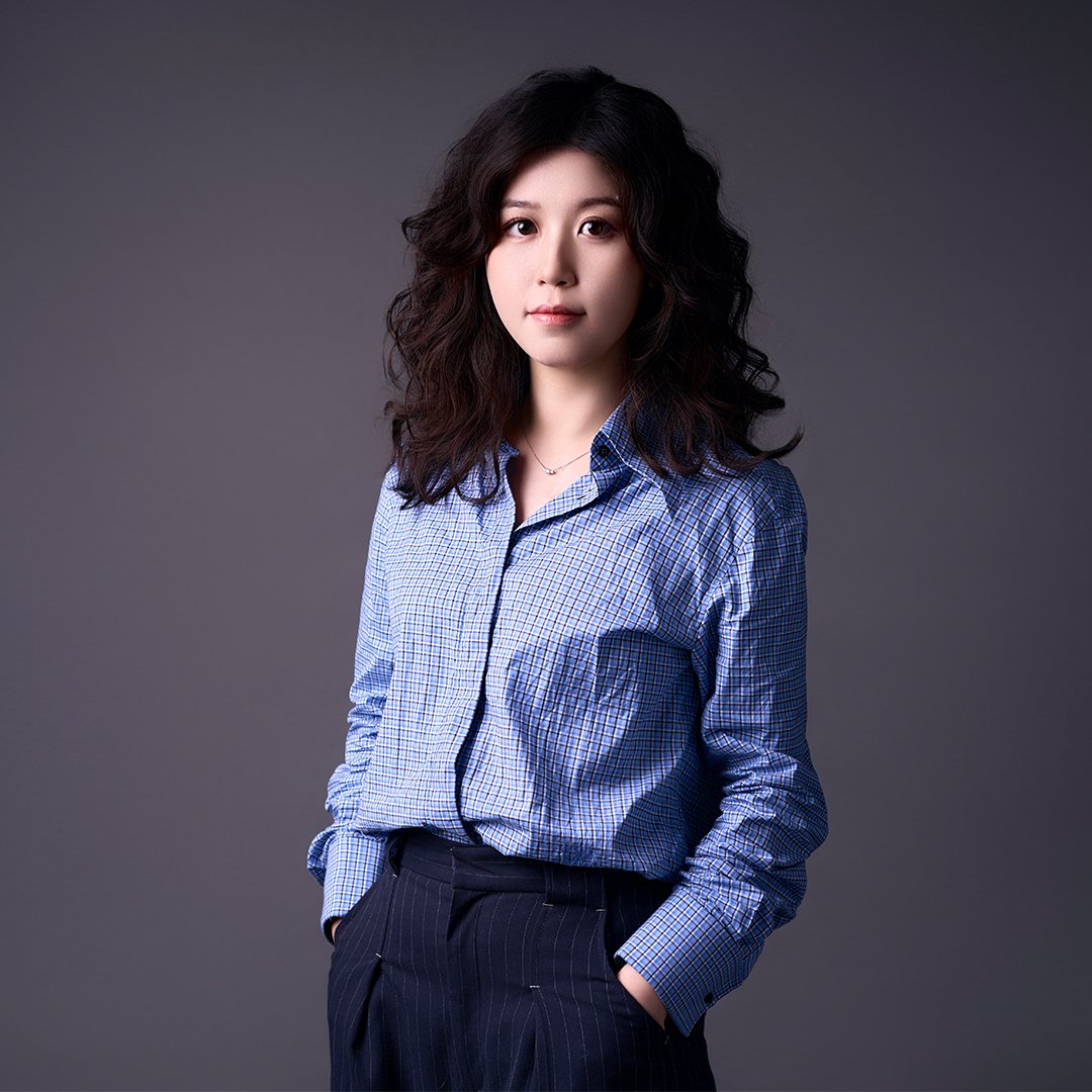 Professional studio portrait of Christine Wang wearing a blue checkered shirt against a gray background.