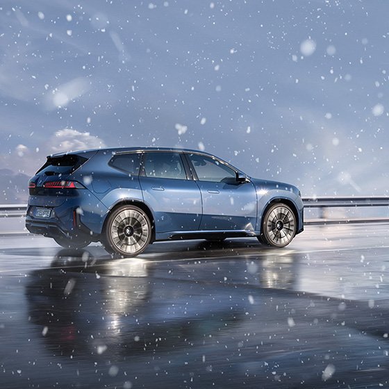 A blue BMW iX3 drives through falling snow.