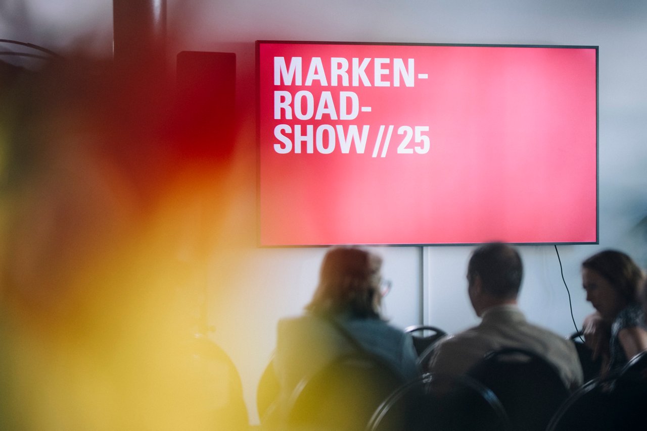 Bild des Screens an den Vorträgen der Marken-Roadshow mit dem Logo