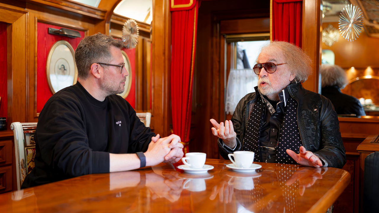 Zwei Personen sitzen an einem Tisch in einem holzvertäfelten Café und unterhalten sich bei Kaffee.