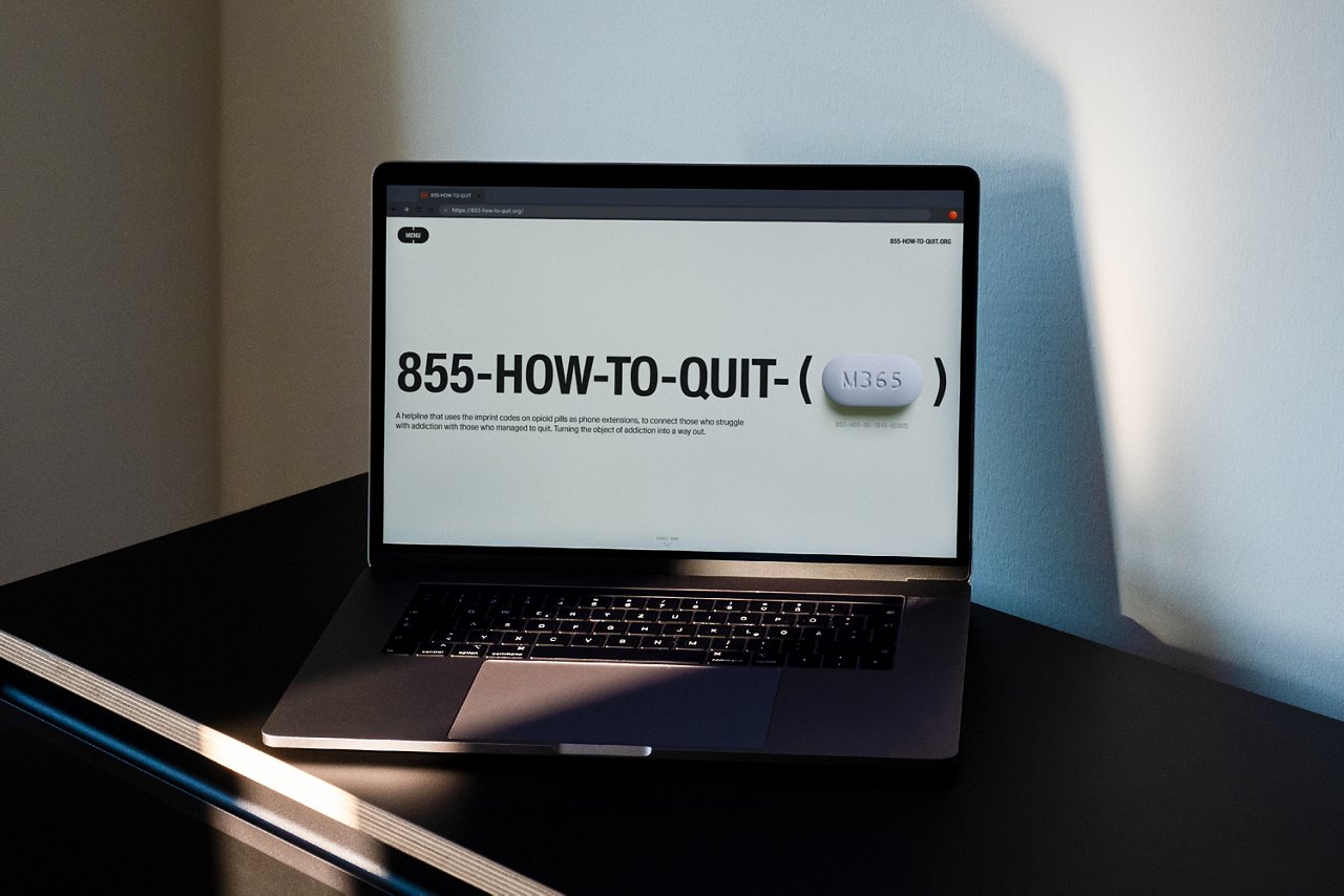 A laptop displays a webpage with the phone number '855-HOW-TO-QUIT', with a white pill in the foreground. The scene is in a minimalist room pointing to an online consultation points out