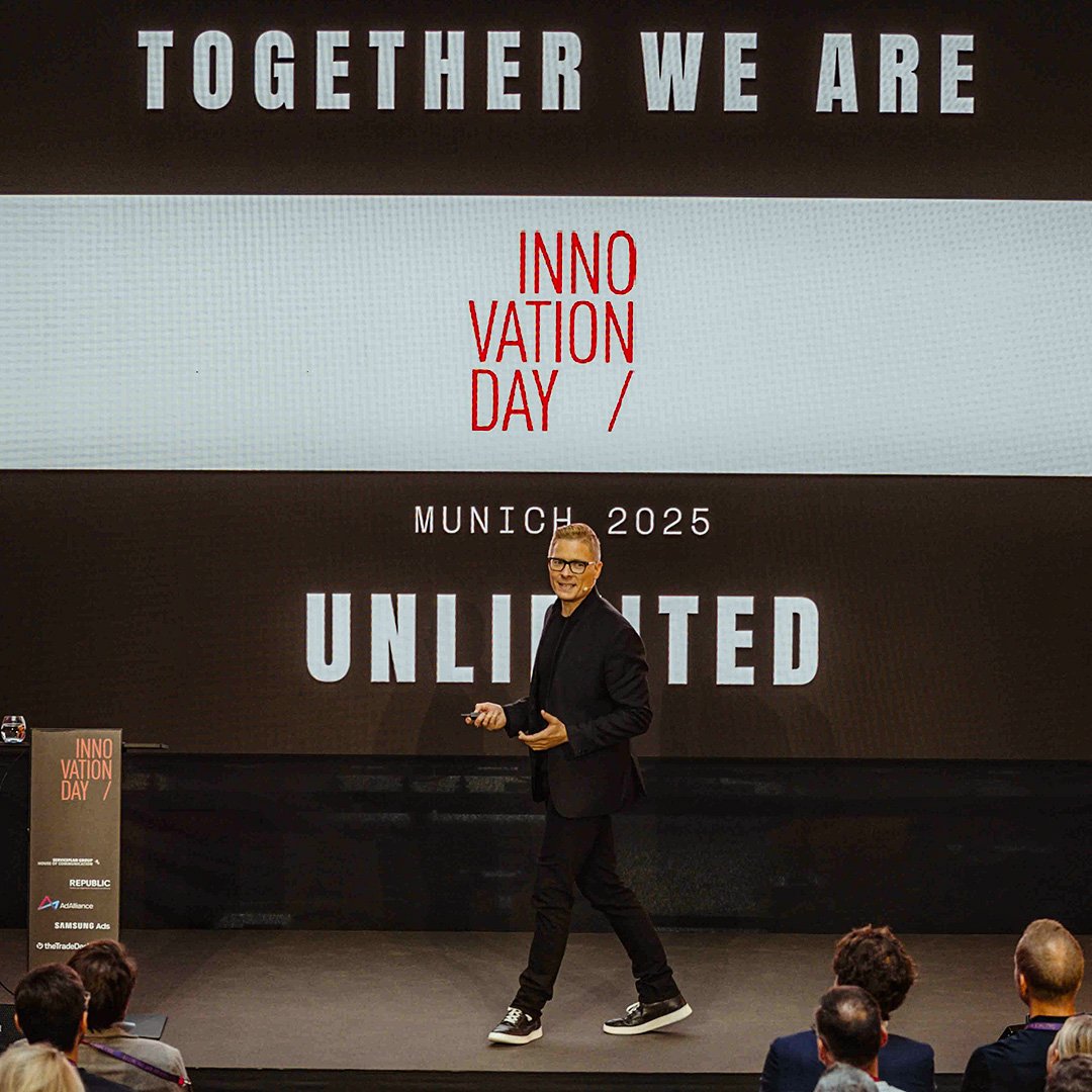 Redner steht auf einer Bühne während einer Präsentation beim Innovation Day in München 2025. Hinter ihm ist eine große Leinwand mit der Aufschrift „Together we are unlimited“.