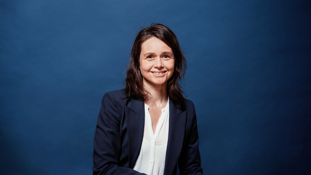 Julia Zimmermann, Managing Partner at Future Marketing: The picture shows a smiling woman with dark brown hair in a blazer and white blouse against a dark blue background.