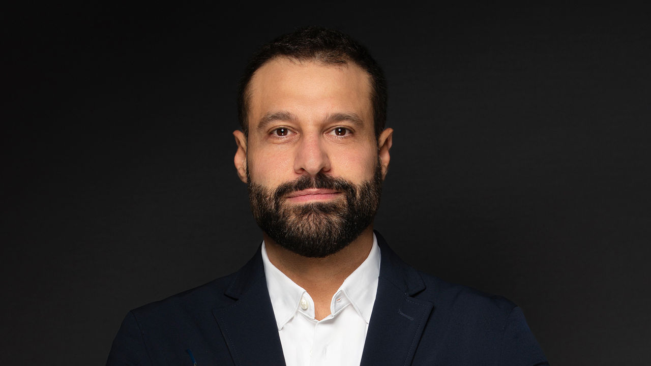 Hicham Soubra, Head of Production at Serviceplan Arabia: A man with dark hair and a beard is wearing a white shirt and dark suit against a black background.