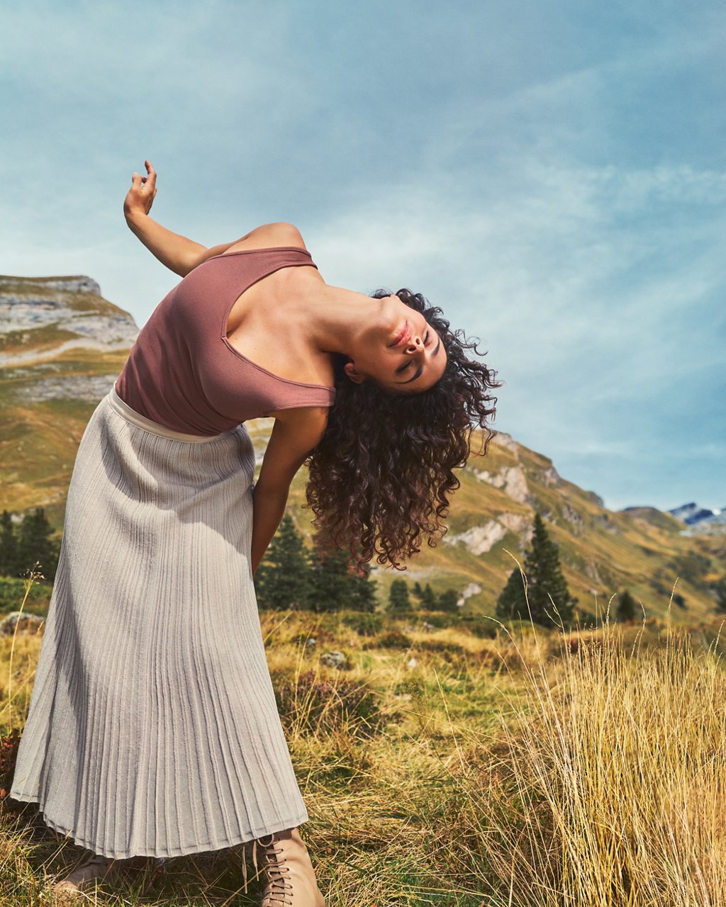 Tanzende Frau vor blauem Himmel in einer alpinen Landschaft