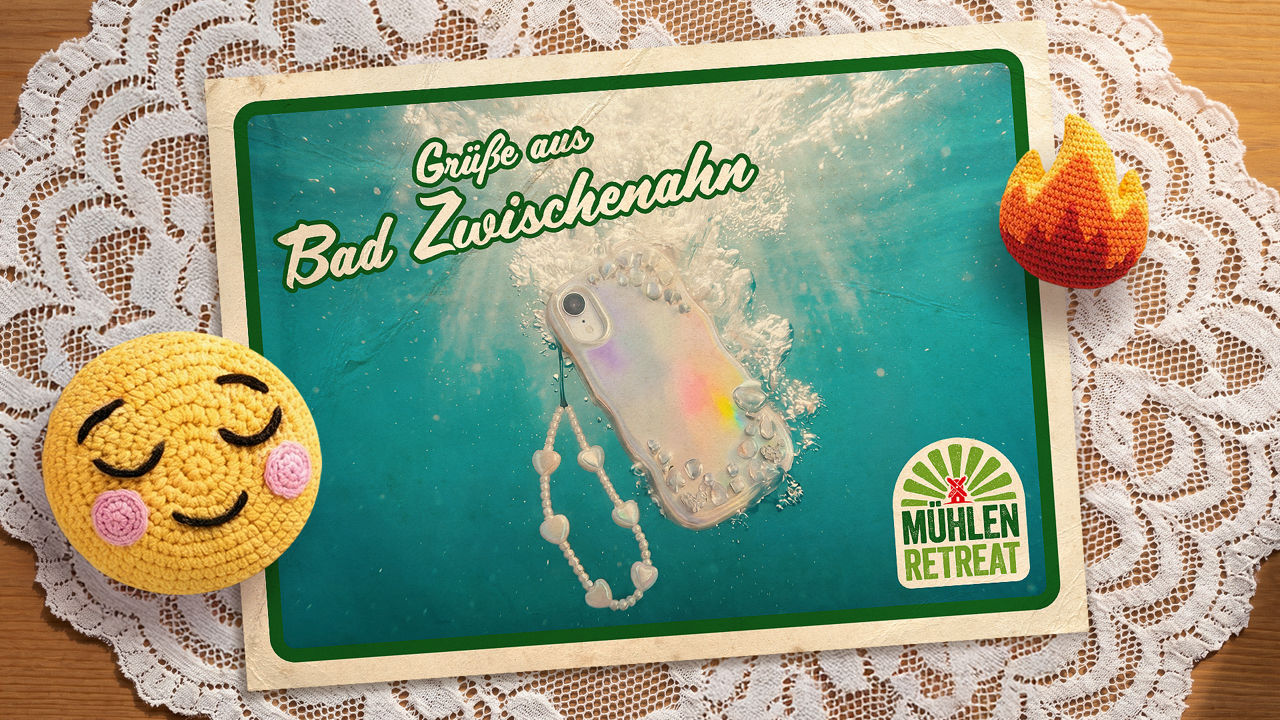 Postkartenmotiv mit der Aufschrift ‚Grüße aus Bad Zwischenahn‘ und einem Smartphone unter Wasser auf einer Spitzendecke.