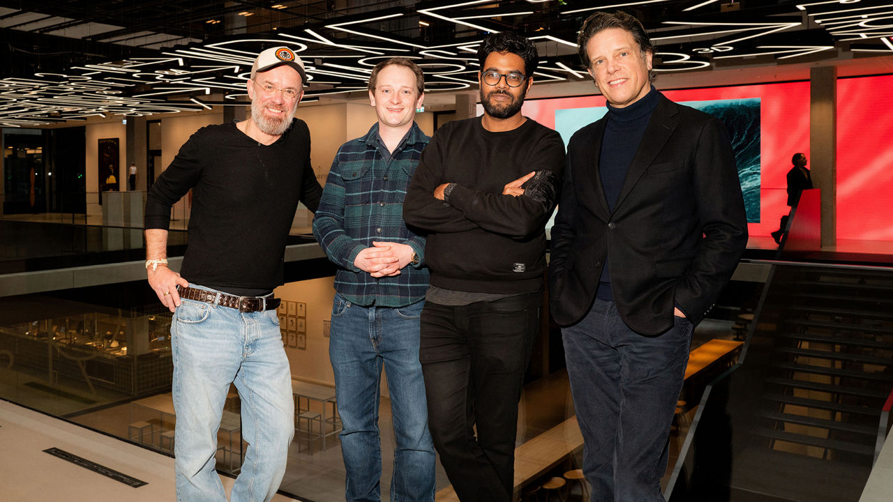 Fyra personer står i en modern interiör med karakteristisk takbelysning och är vända mot kameran.