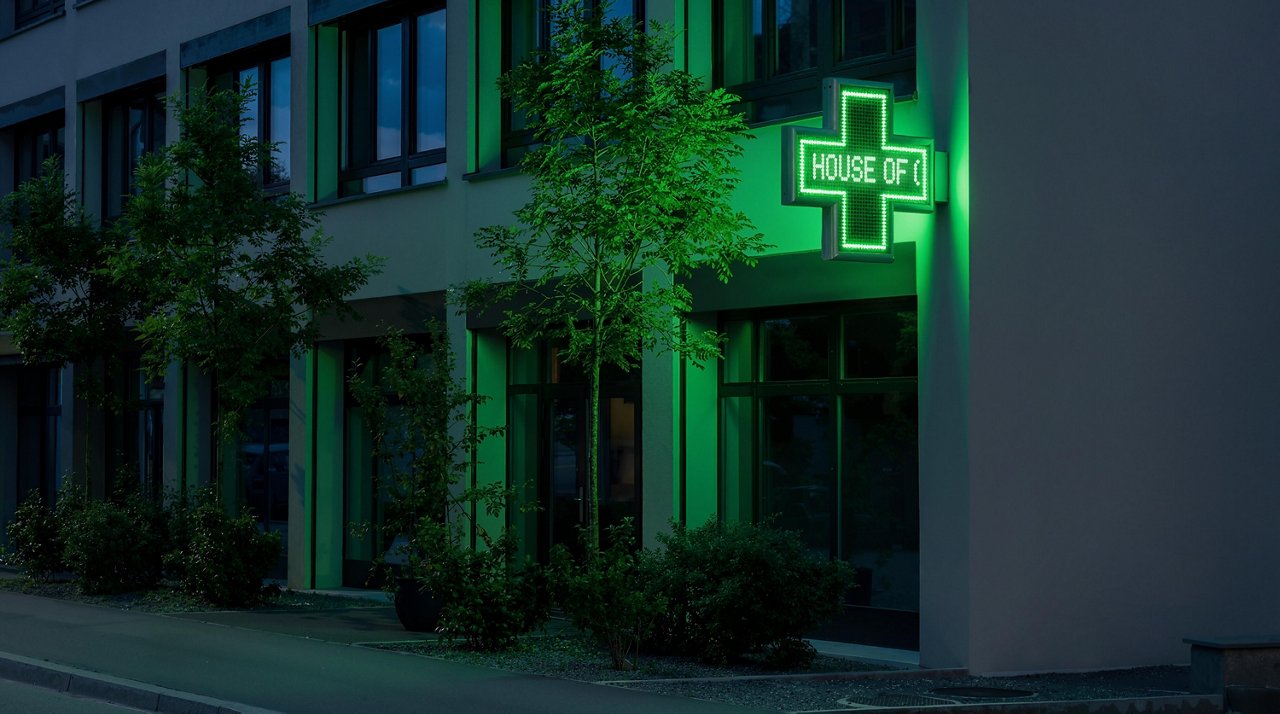 Ein Bild des House of Communication Zürich, auf dem eine gründe Apothekertafel angebracht ist in der Nacht