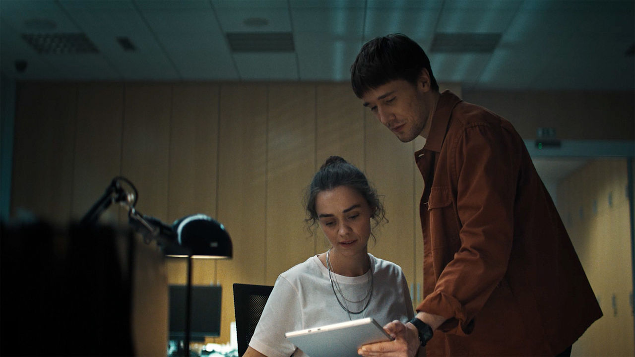 Zwei Personen betrachten gemeinsam ein Tablet in einem Büro mit gedämpfter Beleuchtung.