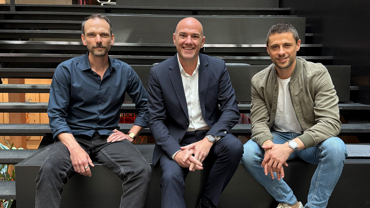 TWELVE CAST mit Benjamin Majeron, Jan Düring und Jochen Werne. Das Bild zeigt drei Männer. Sie sitzen nebeneinander auf einer schwarzen Treppe in einem modernen Innenraum; der Mann in der Mitte trägt einen dunklen Anzug, während die beiden anderen leger gekleidet sind – der linke in einem dunklen Hemd und der rechte in Jeans und einer hellen Jacke.
