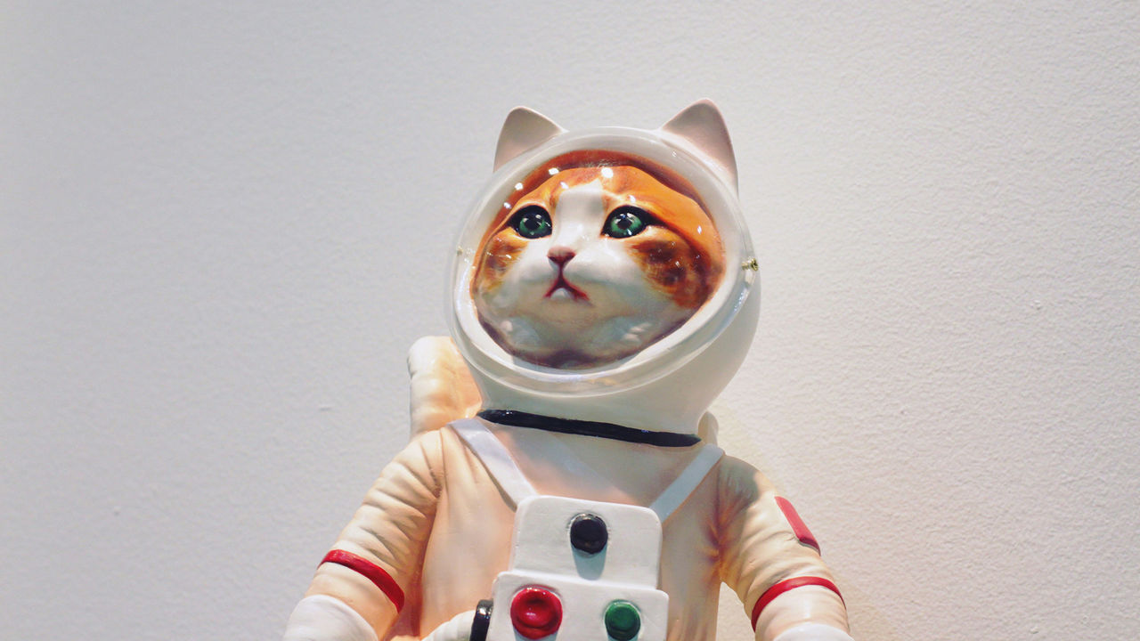 Eine detailreiche Skulptur einer orange-weißen Katze in einem Astronautenanzug mit Helm, die mit neugierigem Blick in die Ferne schaut.