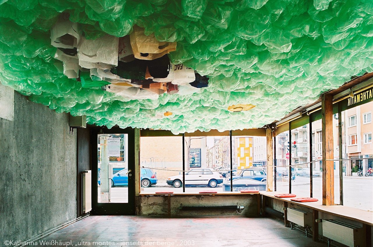 Featured work of art on the talk show "Artpros": Interior view of a commercial space with an artistic ceiling installation by Katharina Weißhäupl made of green and white plastic bags. Large windows offer views of the street