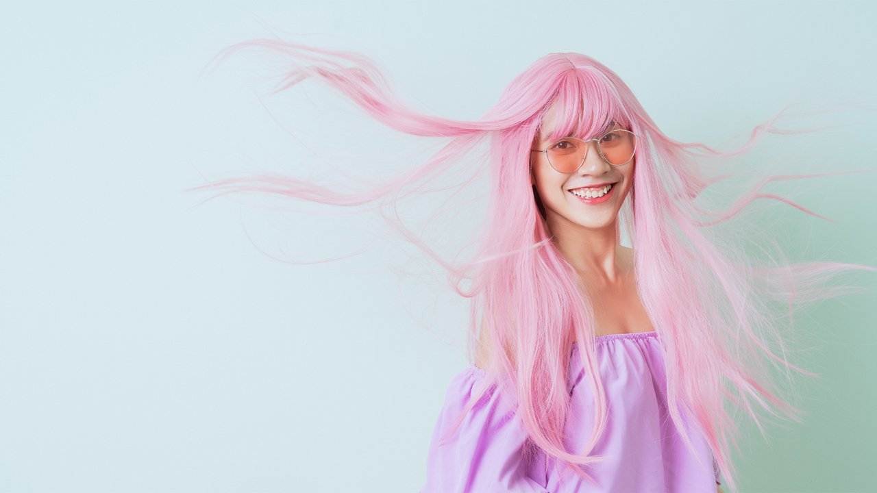 Young woman with flowing pink hair and sunglasses smiling against a light background