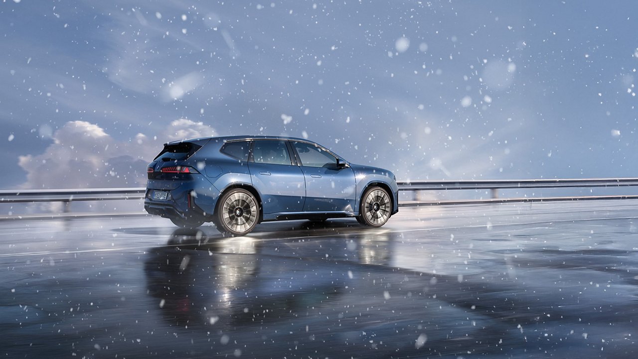 En blå BMW iX3 kör i snöfall.