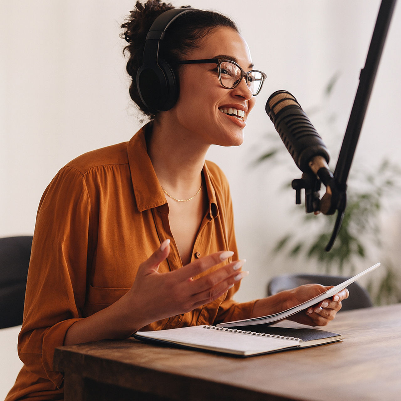 A woman wearing headphones speaks into a microphone while recording a podcast.