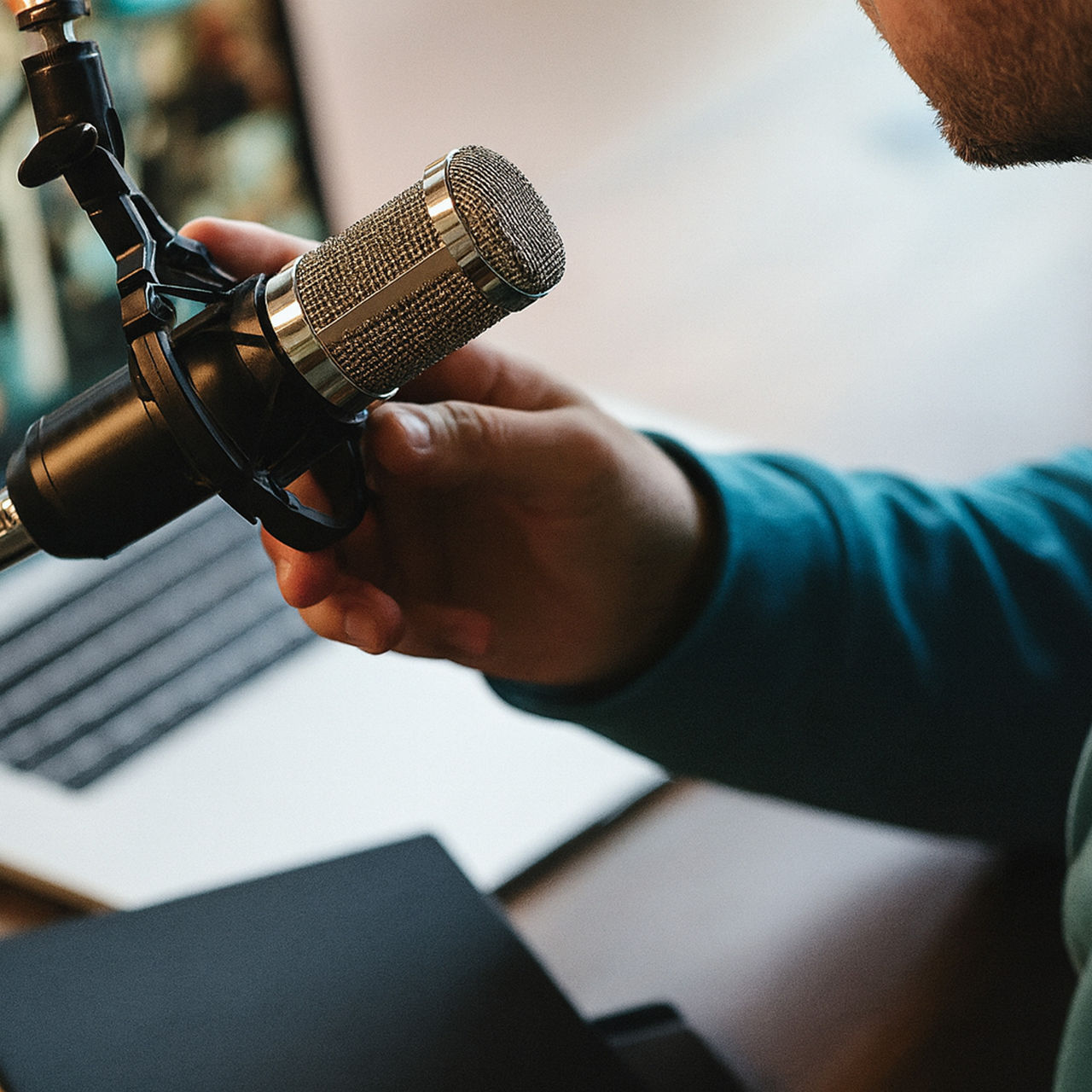 A close-up of a person adjusting a professional microphone next to a laptop during a reciording session