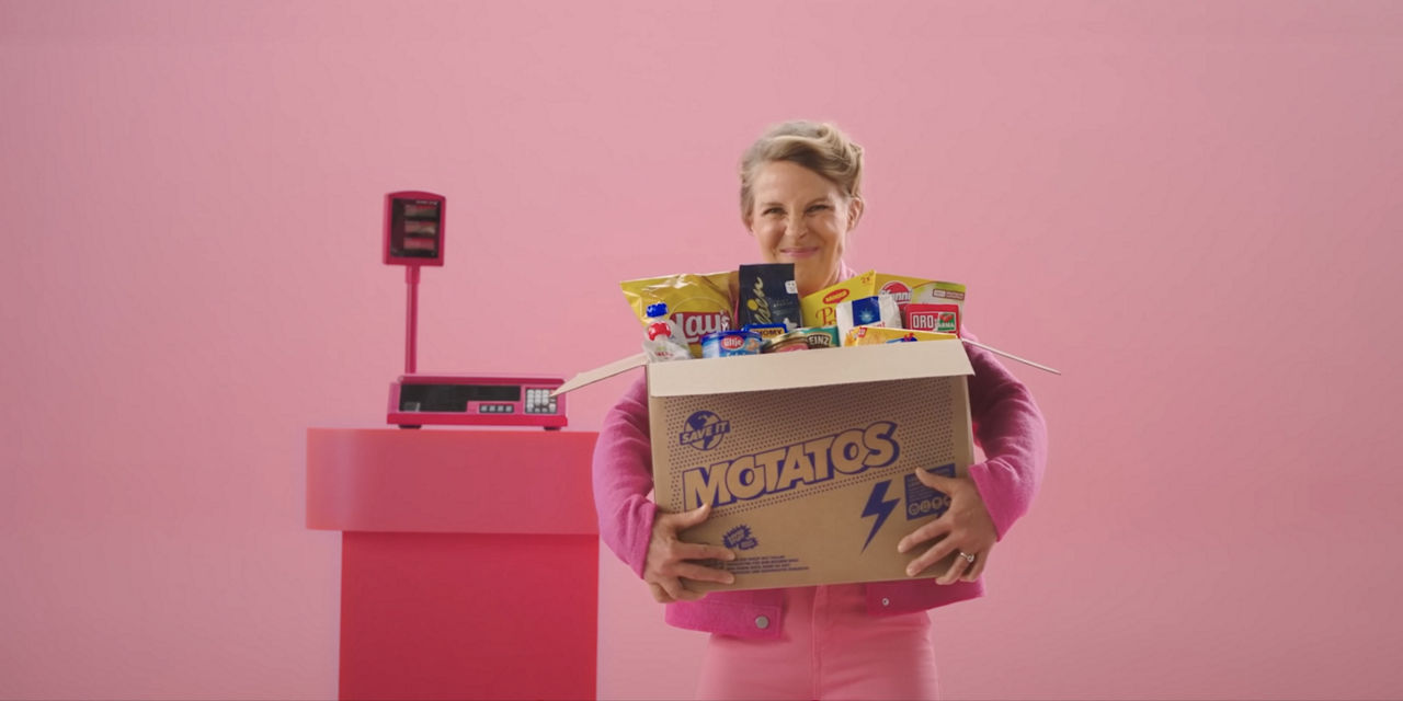 Motatos - Inflation Targeting - A woman in a pink suit happily holds a package of groceries from Motatos. The background is a pink cash register.