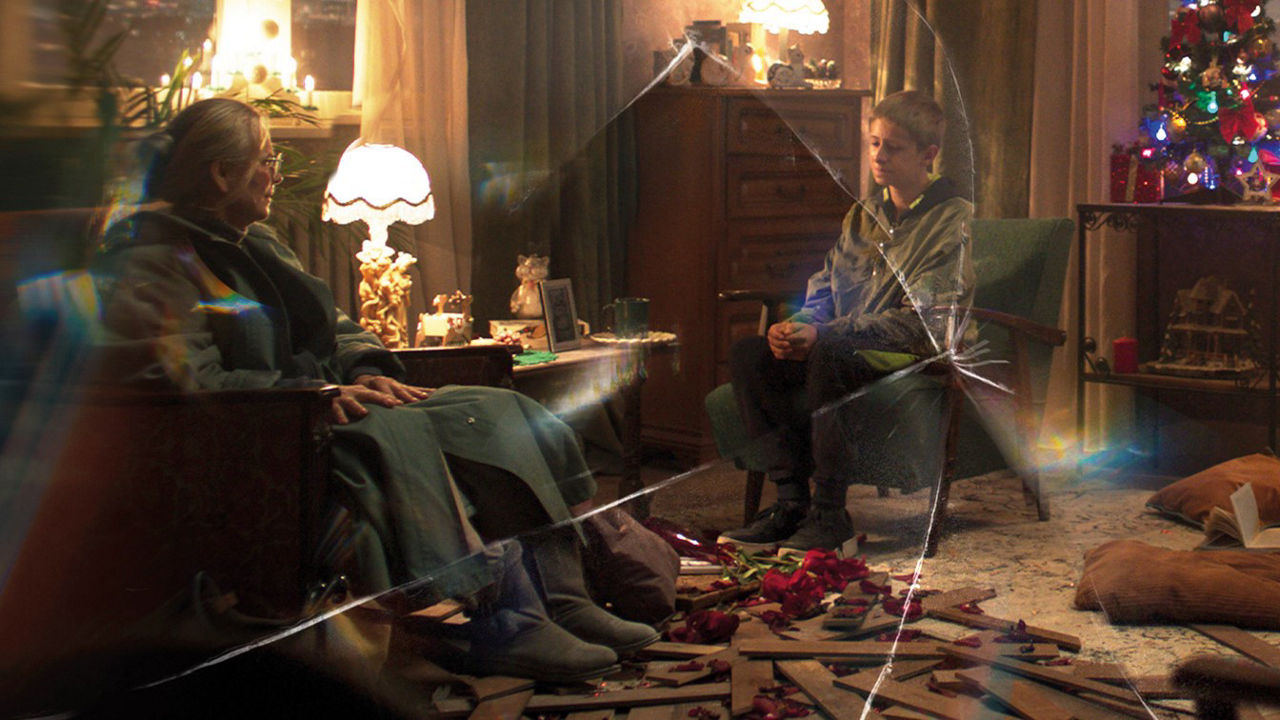Sad boy and elderly lady sit behind a cracked pane of glass at Christmas