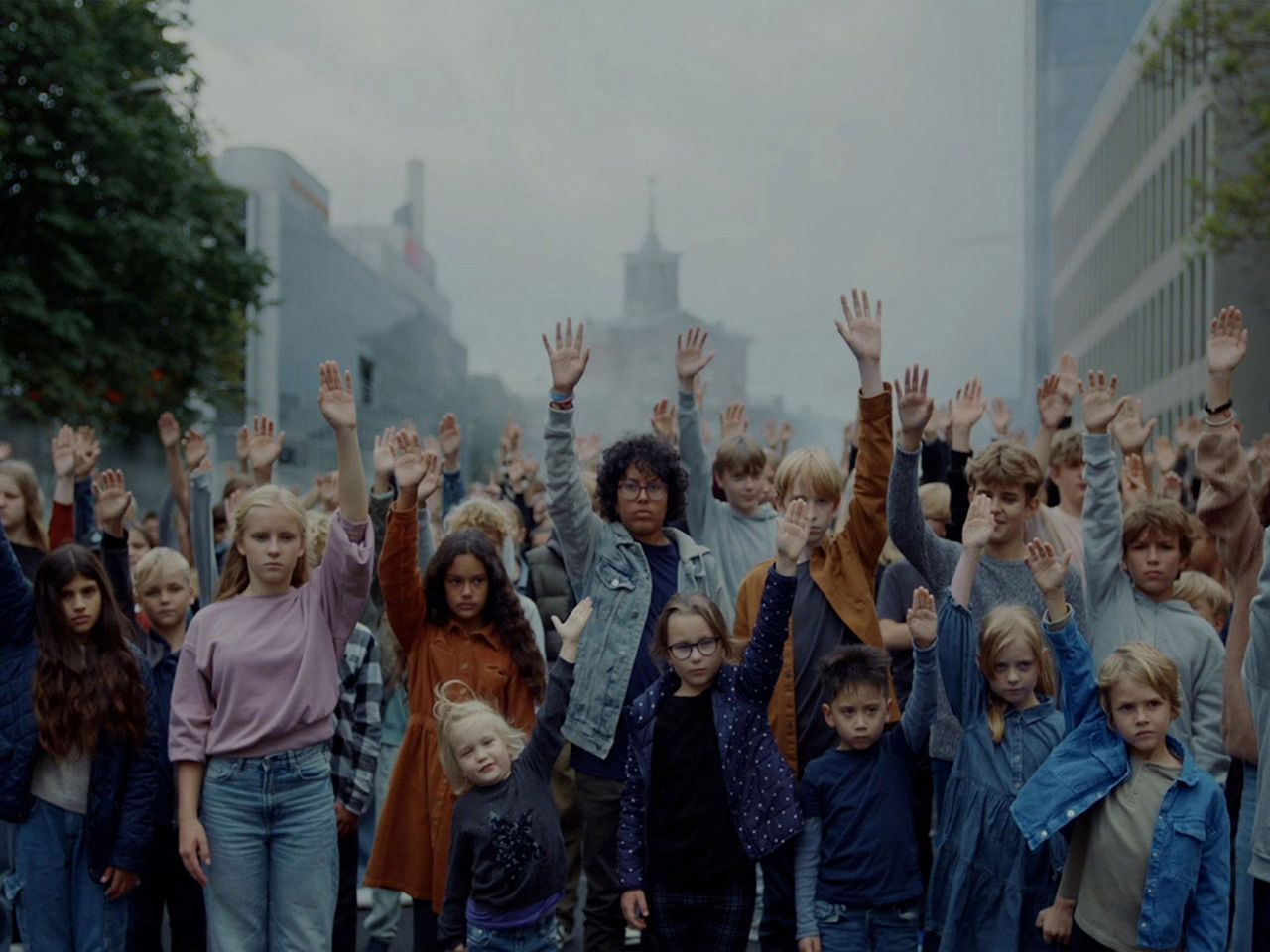 PENNY - The Kids - A large group of children of different ages and genders stand together with serious expressions. Everyone raised their right arm which symbolized giving children and young people a voice and listening to them