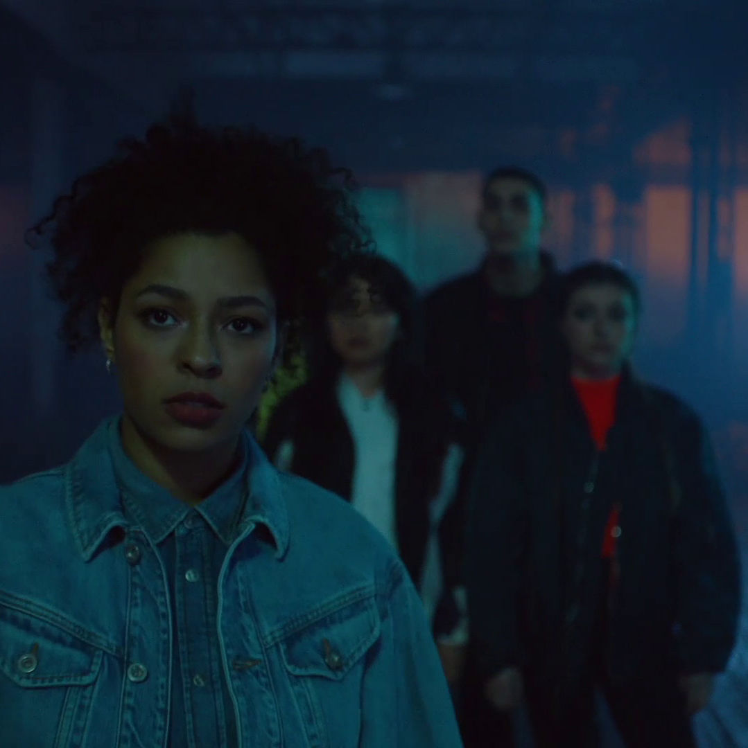 A group of young people stand in a dark, neon-lit environment
