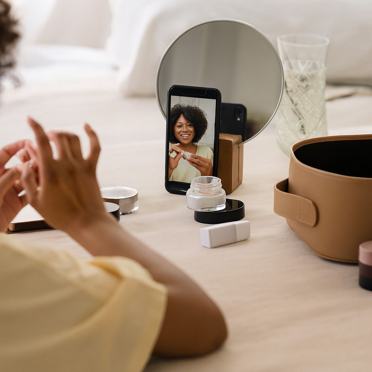 A woman recording a beauty tutorial with skincare products in front of a mirror using her smartphone.