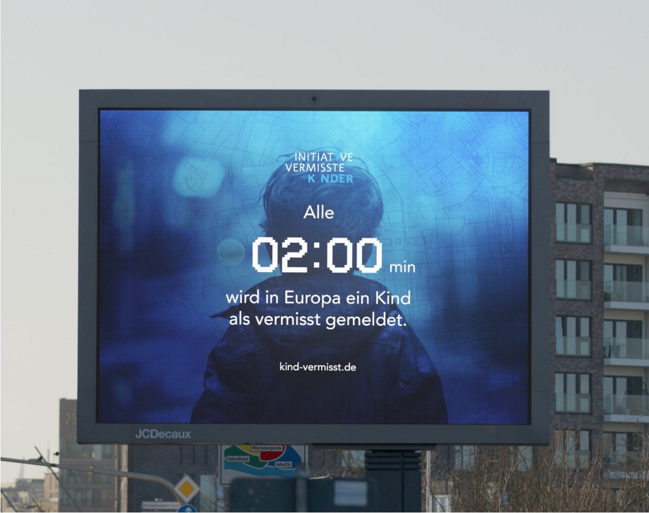 Digital billboard displaying a campaign by the Initiative for Missing Children. In the background, a child is seen from behind. The text in white reads: 'Every 02:00 minutes a child is reported missing in Europe.' Below it is the website 'kind-vermisst.de'.