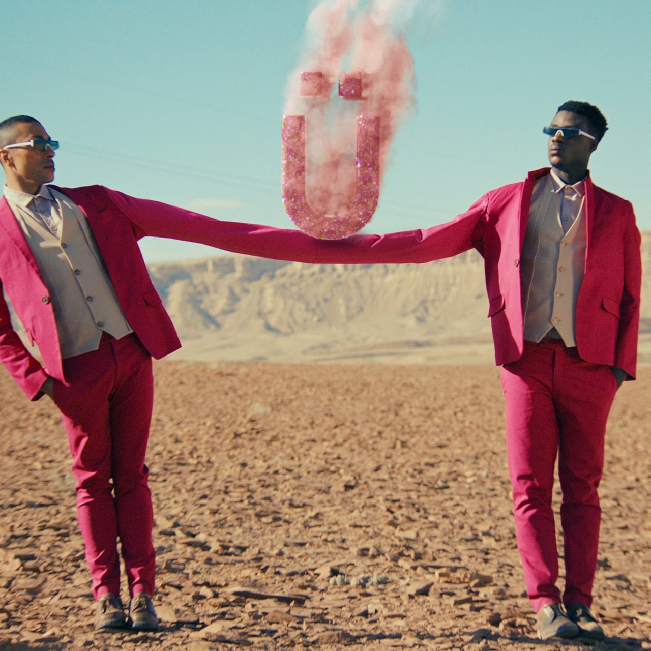 two men holding each others hand, connected with an Ü, für ÜberCreativity 