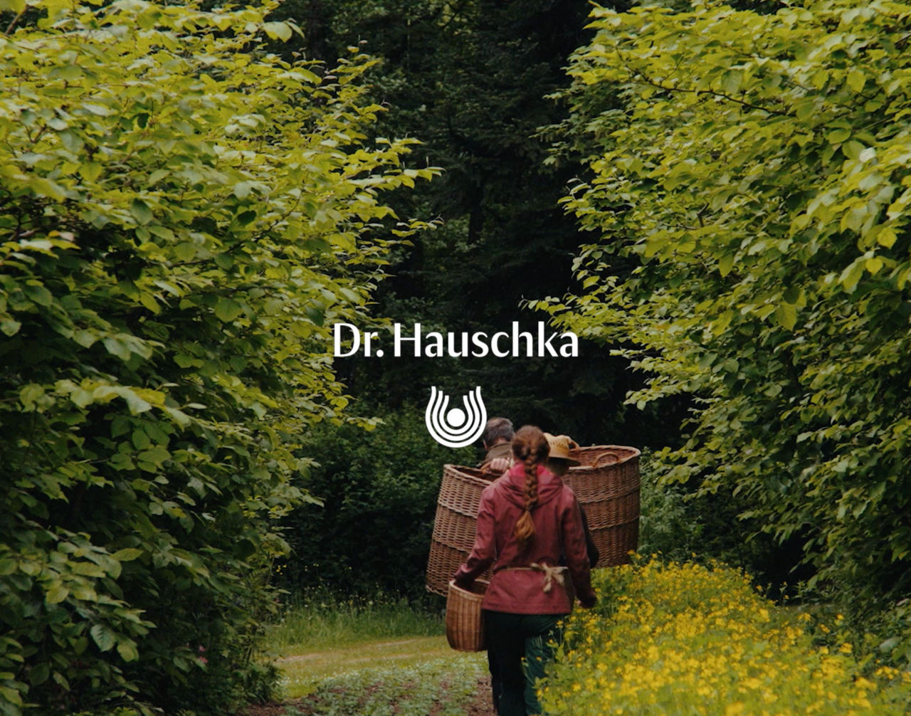 A person with a backpack on a forest trail surrounded by trees, featuring the Dr. Hauschka logo.