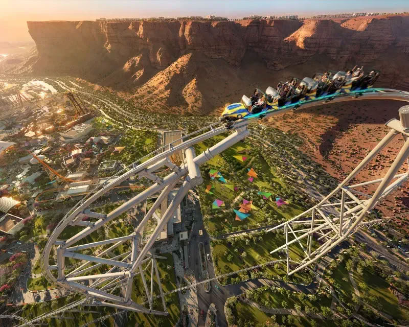 Qiddiya City attractions section highlighting theme parks, sports venues, and entertainment experiences, with an aerial view of a large-scale amusement park integrated into a mountainous landscape