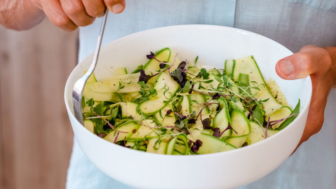 Patient hält eine Salatschüssel mit Zucchini, Sojasprossen und frischem Gemüse als Beispiel für gesunde Ernährung bei chronischer Nierenerkrankung (CKD)