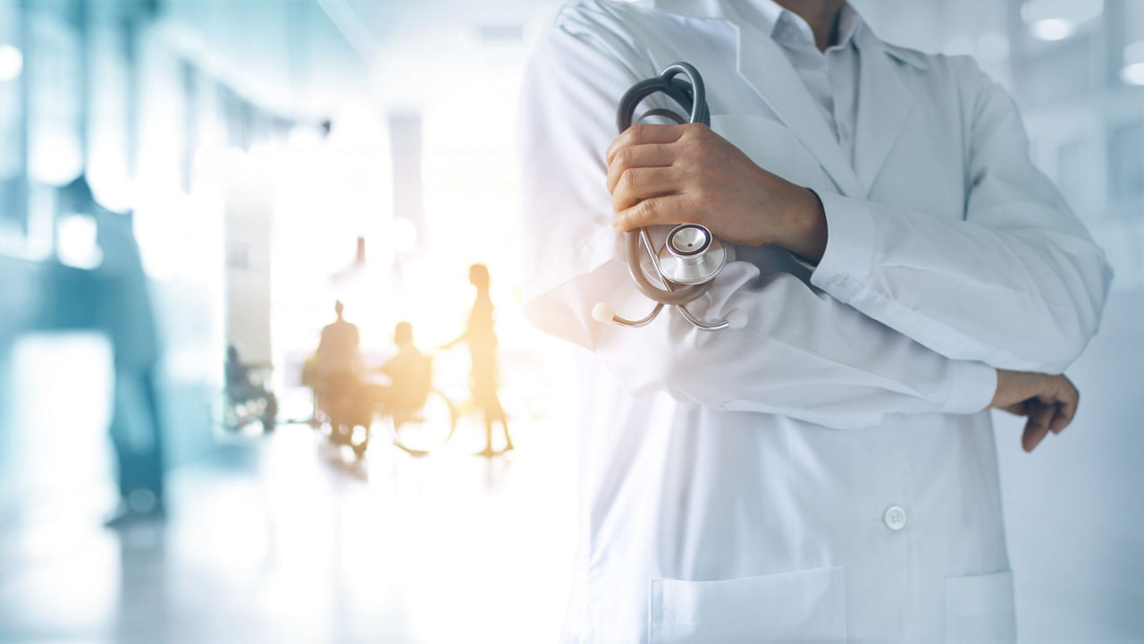Mediziner im Krankenhaus mit Stethoskop in der Hand und Patienten im Hintergrund