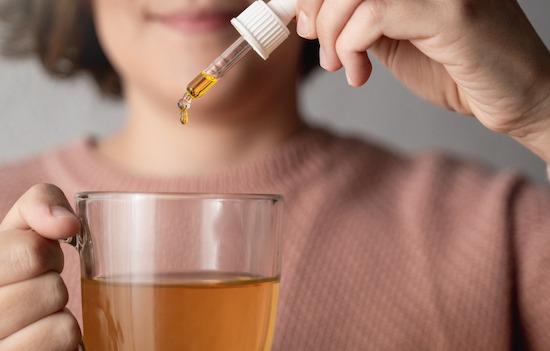 Cbd hemp oil - Woman taking cannabis oil in tea cup - Focus on drop