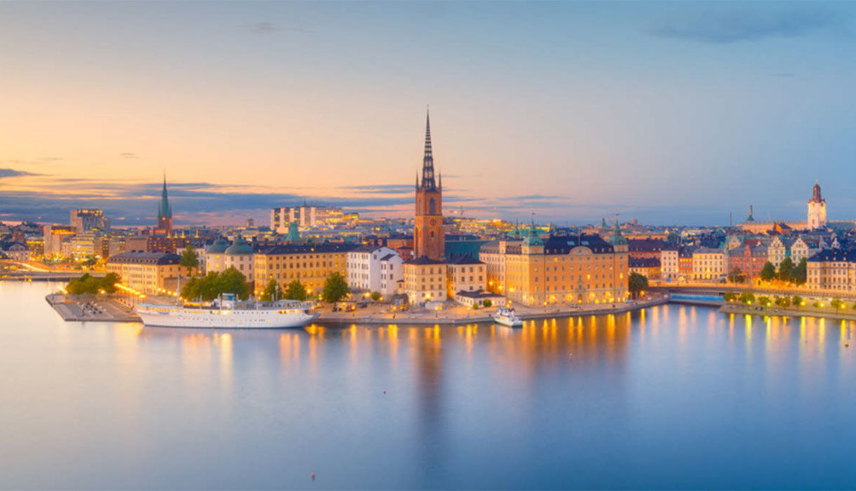 Panoramaansicht der Altstadt von Stockholm mit der Riddarholmen-Kirche am Wasser bei Dämmerung.