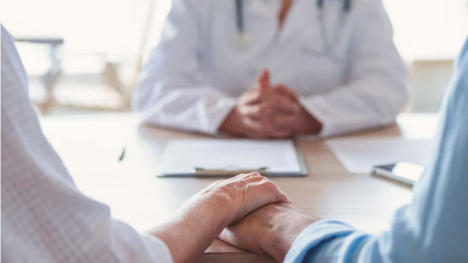 Zwei Menschen halten sich die Hand während einer ärztlichen Konsultation.