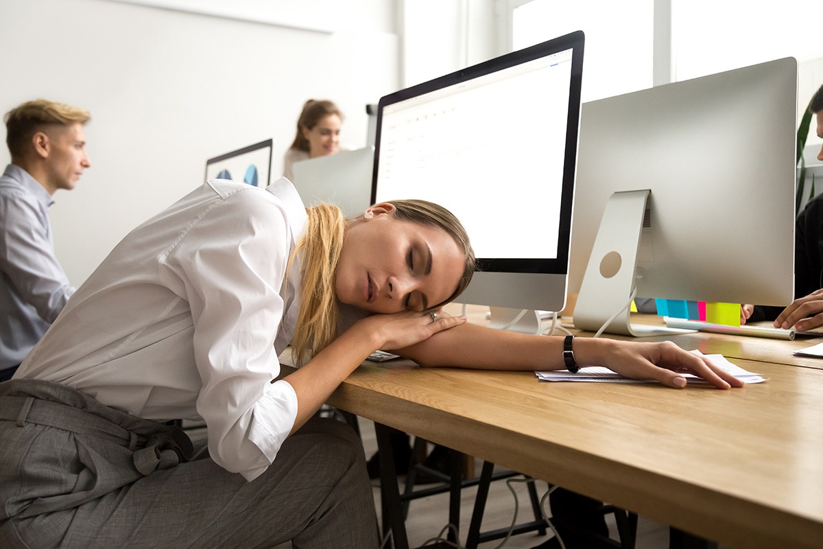 Restless young businesswoman sleeping at work desk, tired or bored female employee lying asleep at workplace at break, exhausted overworked office worker feeling lack of sleep or fatigue having nap