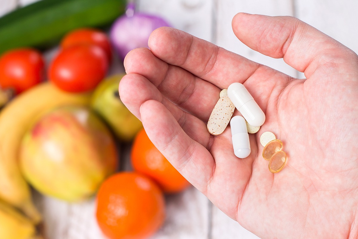 Hand with dietary supplements on fruity background