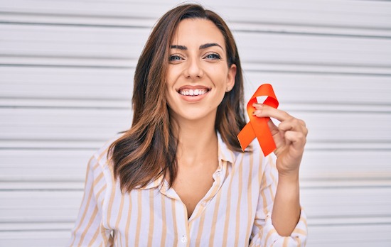 Young hispanic woman smiling happy holding awareness orange ribbon standing at the city.