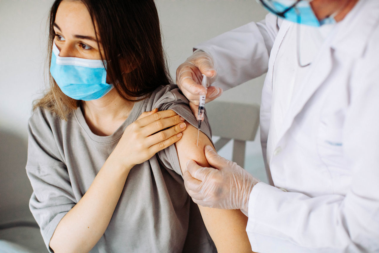 Young woman with face mask getting vaccinated, coronavirus, covid-19 and vaccination concept. Closeup of a nervous woman and her doctor wearing face masks and getting a vaccine shot in a doctor's office