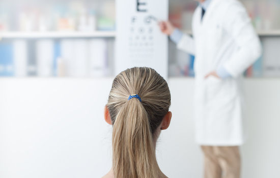 Young woman in the optometrist office examining her eyesight, he is pointing at the chart, eye care concept