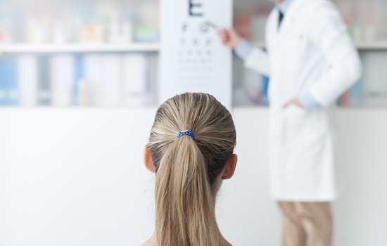 Young woman in the optometrist office examining her eyesight, he is pointing at the chart, eye care concept