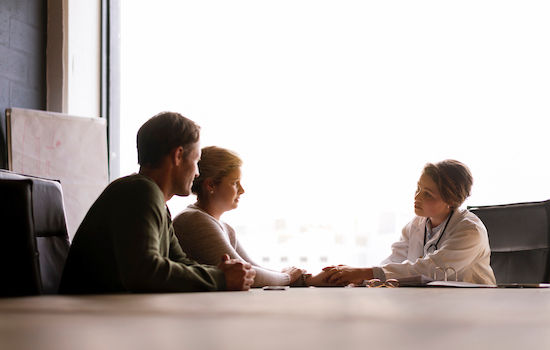 A photo of female doctor comforting couple. Mid adult partners consulting from medical professional. They are at doctor's office.